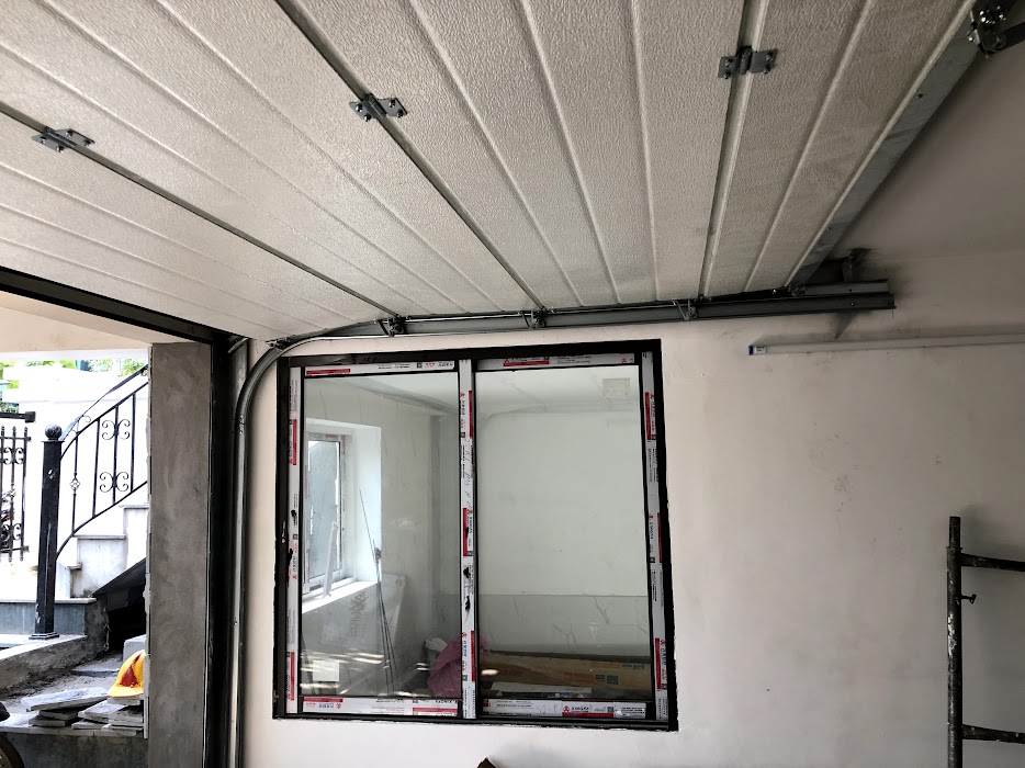 Cửa cuốn trần gara đang lắp đặt bên trong nhà, phía sau là cửa sổ kính khung nhôm mới thi công